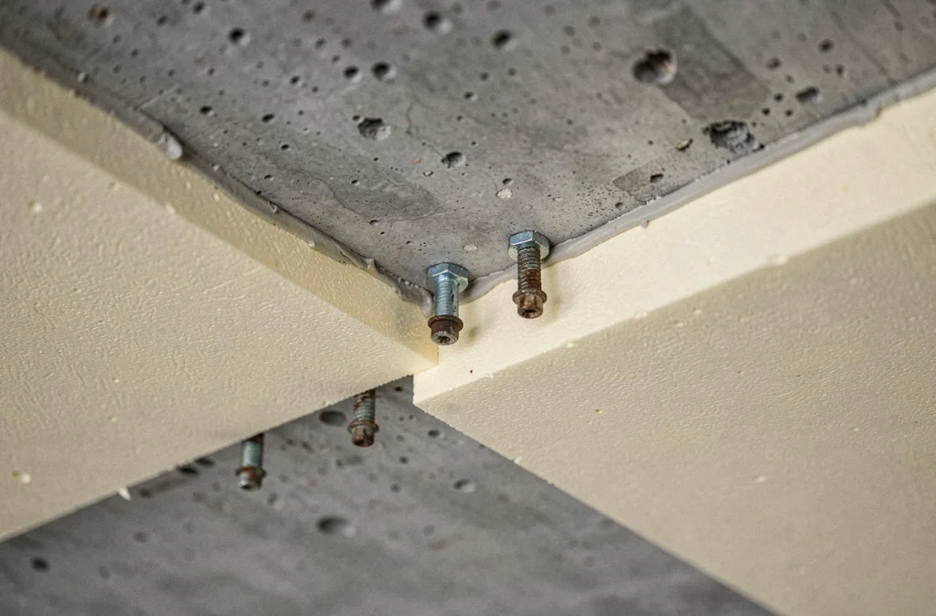 Gros plan sur un panneau isolant polyuréthane fixé mécaniquement à un plafond béton de garage