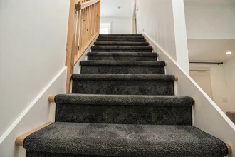 Moquette antidérapante grise installée sur les marches d'un escalier moderne en bois dans un intérieur contemporain
