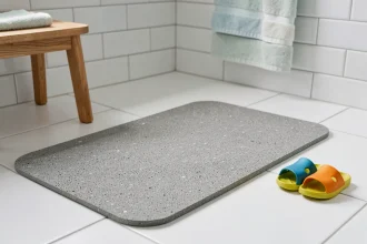 Tapis en diatomite gris posé sur carrelage blanc dans une salle de bain, avec de petites chaussons colorés d'enfant à côté, soulignant la sécurité et le confort
